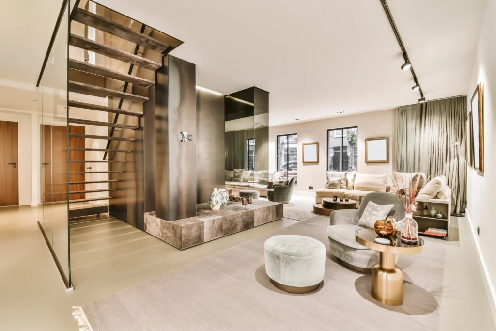 Sala moderna bajo tendencias de interiorismo y diseño de interiores con sofá beige, sillón gris y acabados metálicos.