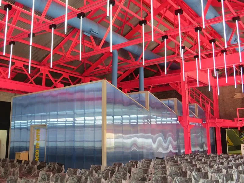 Interior de un museo o espacio cultural con vigas rojas, ductos azules y una estructura central moderna de arquitectura y construcción.