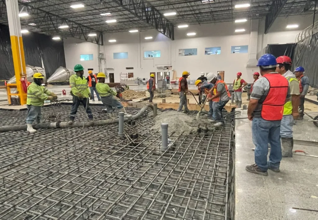 Equipo de trabajadores de arquitectura y construcción vertiendo concreto en una losa de cimentación con estructura de varilla.