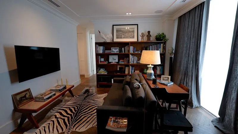 Perspectiva de diseño de departamentos que incluye un sofá gris, tapete de piel y una zona de estudio iluminada.