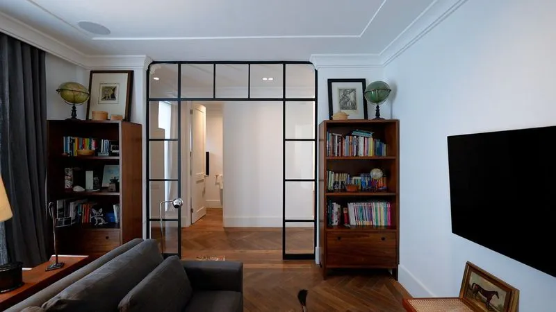 Detalle de diseño de departamentos mostrando una estancia con suelo de espiga y una gran puerta de vidrio industrial.