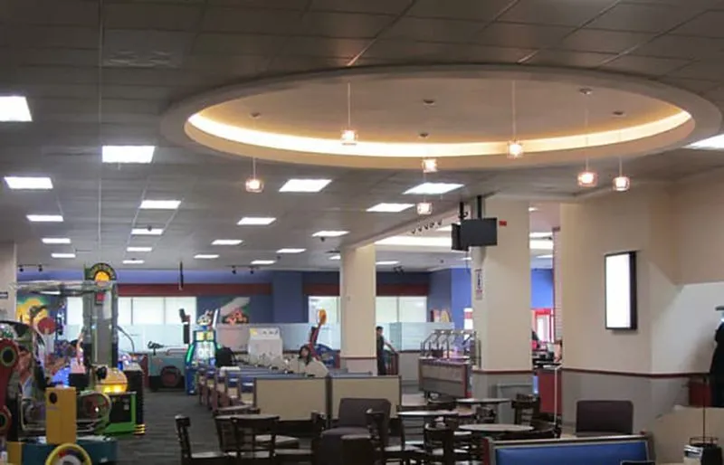 Vista de un salón con mesas de madera y una estructura circular en el techo de donde cuelgan lámparas pequeñas de cristal