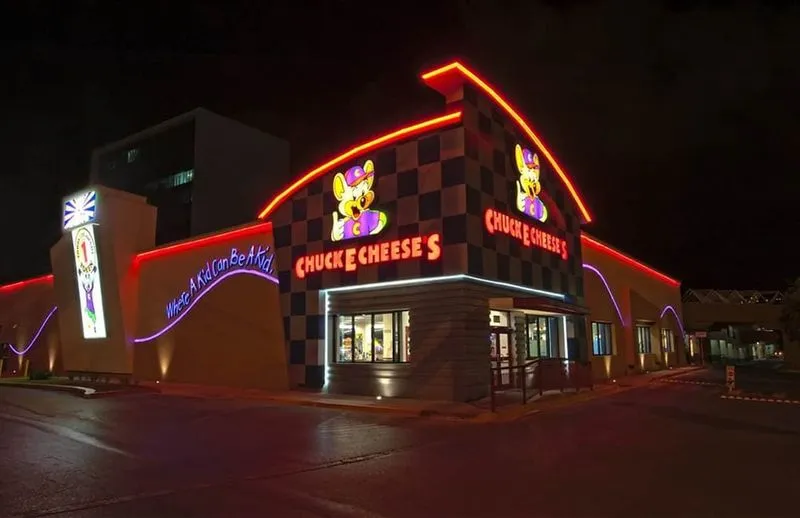 Exterior nocturno de un centro de juegos con luces rojas y azules resaltando las siluetas del edificio y sus logotipos
