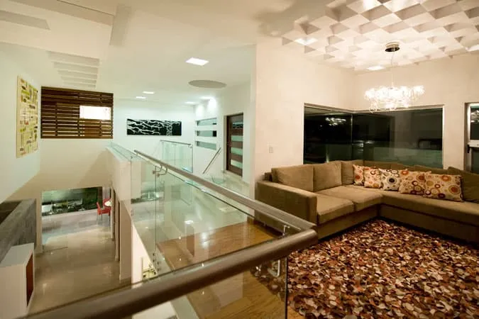 Vista panorámica de sala familiar con acabados de lujo y barandales de cristal en diseño y construcción de casas actuales.