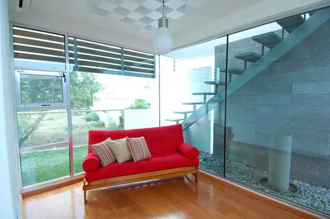 Sala moderna con sofá rojo y ventanales amplios que muestran una escalera exterior en diseño y construcción de casas.