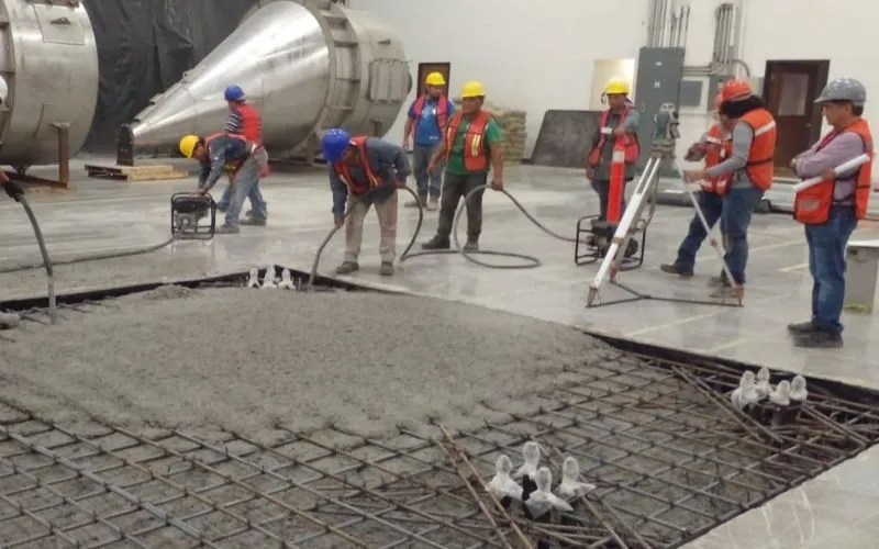 Personal de obra utilizando vibradores de inmersión en parrillas de acero para eliminar burbujas de aire en el concreto.