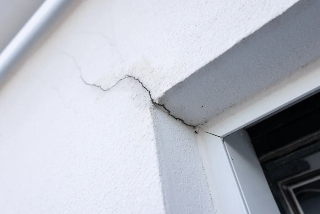 Fotografía de la esquina de una ventana en una construcción color blanca que ya presenta fisuras y grietas.