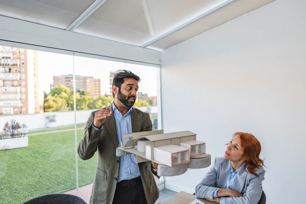 Arquitecto presenta una maqueta arquitectónica de un proyecto residencial a una colega.