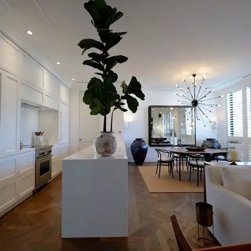 Cocina y comedor diseñados por un despacho de arquitectos, con isla blanca, planta alta y lámpara moderna.