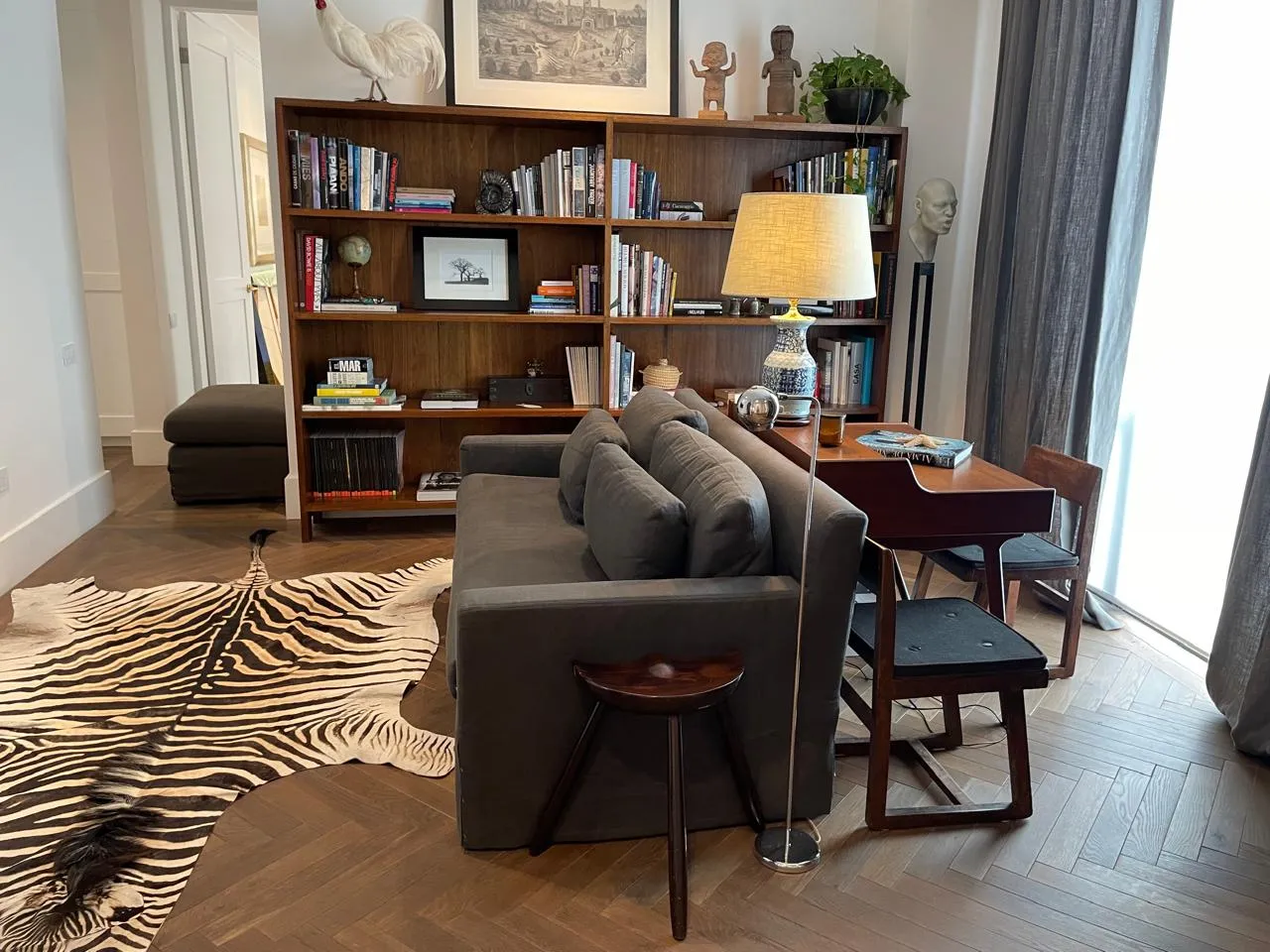 Estudio decorado por un despacho de arquitectos con amplio librero de madera, sillón oscuro y alfombra de cebra.