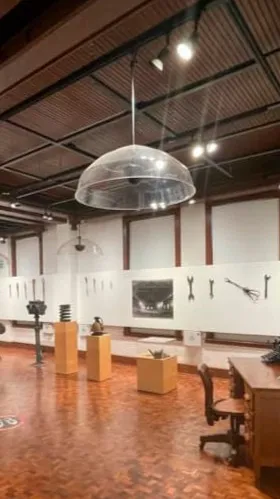Sala de exhibición cultural con herramientas expuestas en la pared diseñada por un despacho de arquitectos.