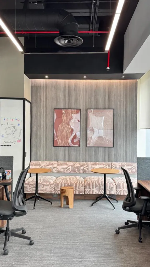 Área de coworking con sillones estampados y mesas redondas de madera diseñada por un despacho de arquitectos.