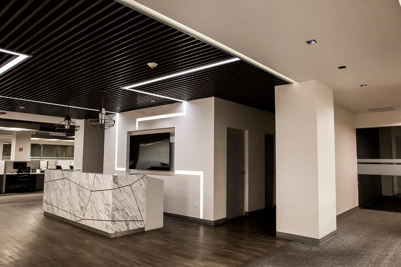Recepción de oficinas de lujo con mostrador de mármol y diseño de iluminación lineal, obra de un despacho de arquitectos.
