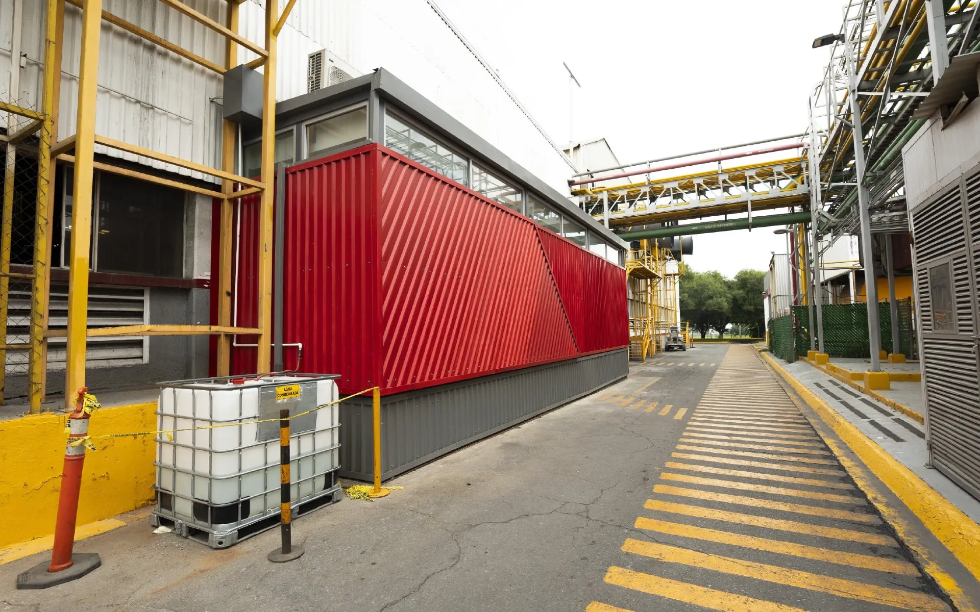 Innovador módulo de oficinas industriales con fachada roja vibrante en un patio de fábrica, diseñado por un despacho de arquitectos.