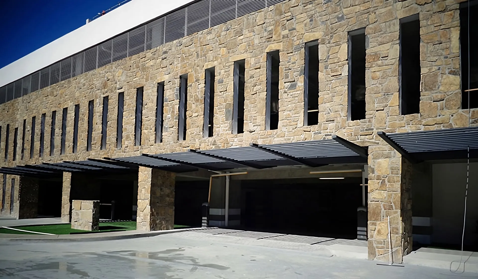 Fachada de complejo residencial con muros de piedra y techos de cocheras, diseñada por un despacho de arquitectos.