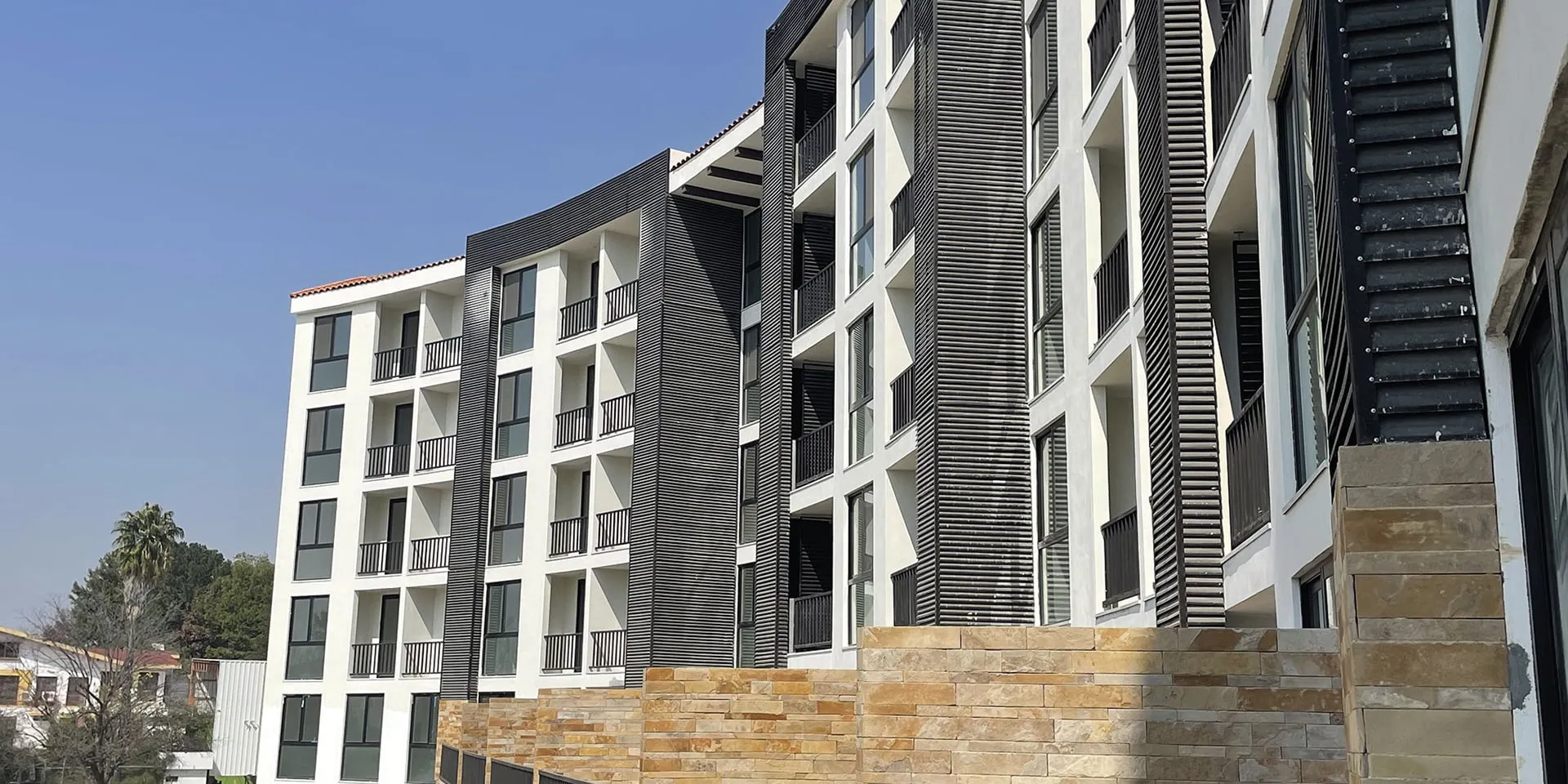 Edificio residencial moderno con balcones negros y fachada curva de estuco blanco.