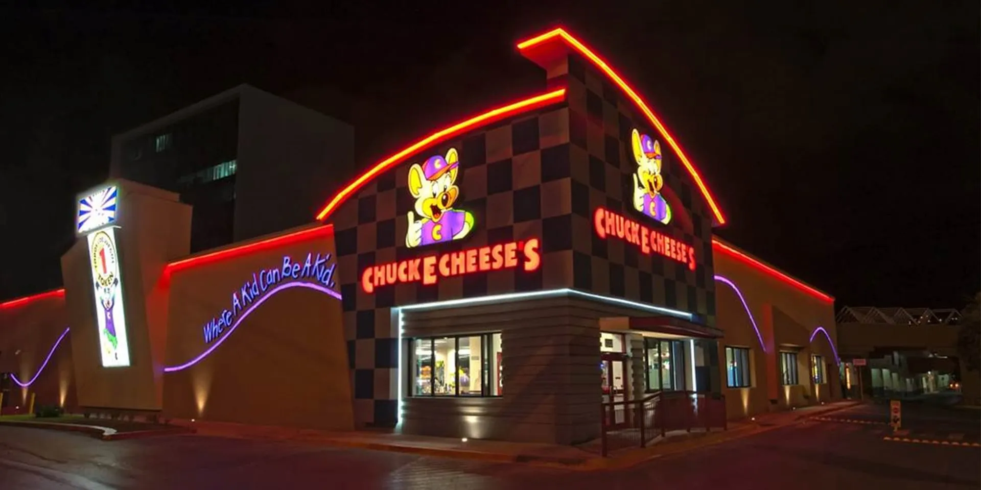Fachada de Chuck E. Cheese's iluminada con luces de neón en la noche.