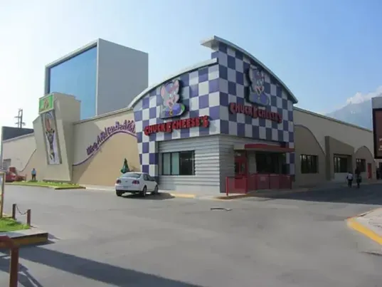 Vista diurna de la fachada de Chuck E. Cheese's con patrón de tablero de ajedrez azul y blanco.